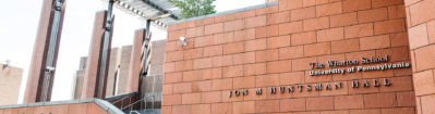 The image shows the exterior of Jon M. Huntsman Hall at the Wharton School, University of Pennsylvania, featuring modern brick architecture.