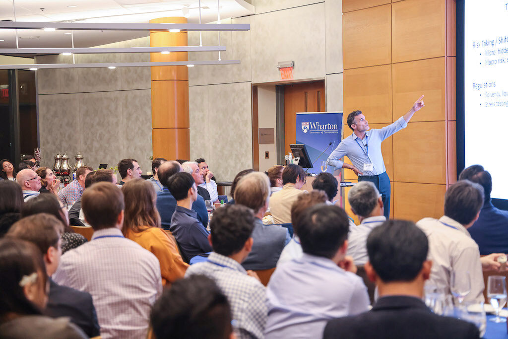 Keynote speaker Thomas Philippon points up to a screen while presenting to an audience.