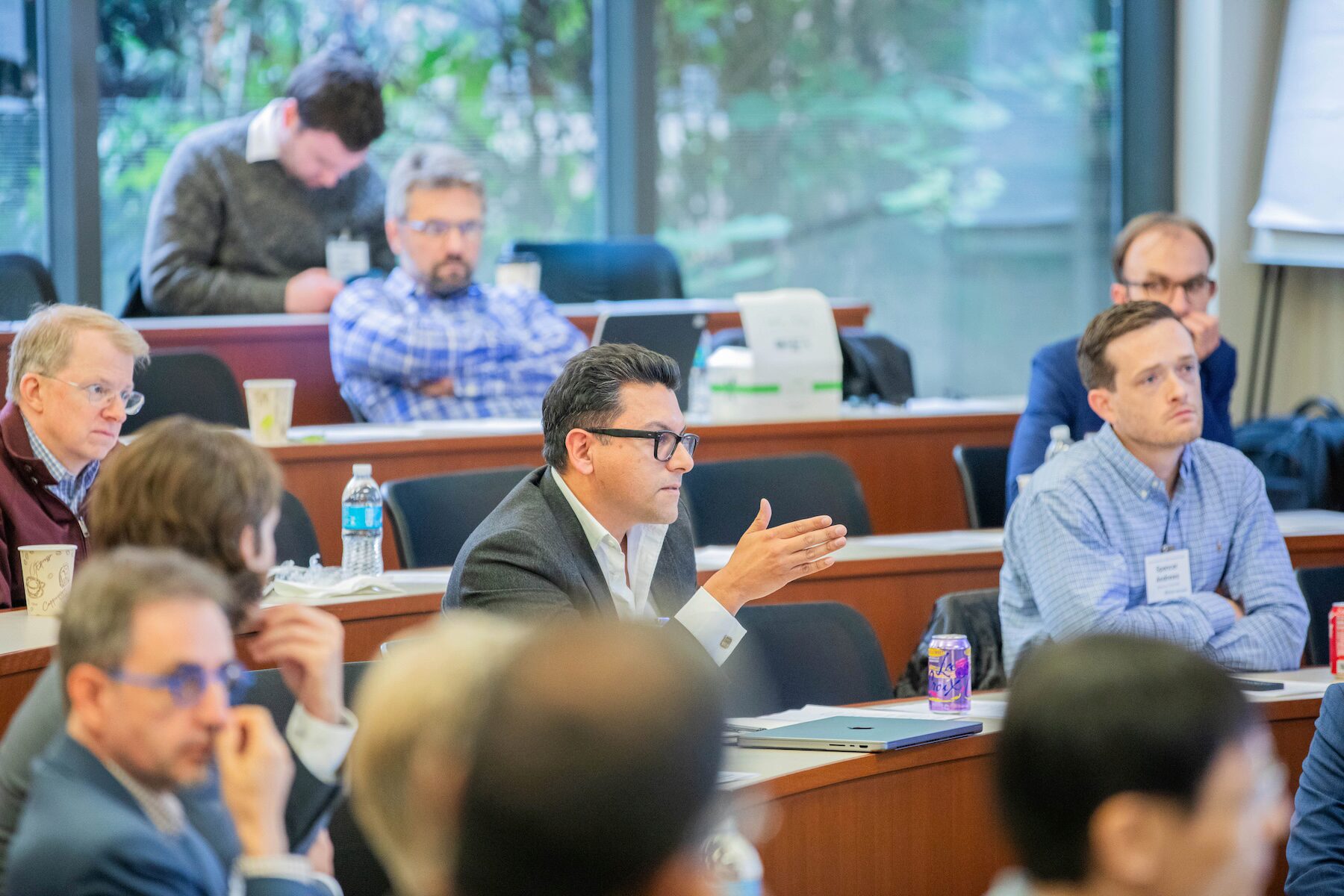 An audience member in a lecture hall motions with his hand while addressing someone off-camera