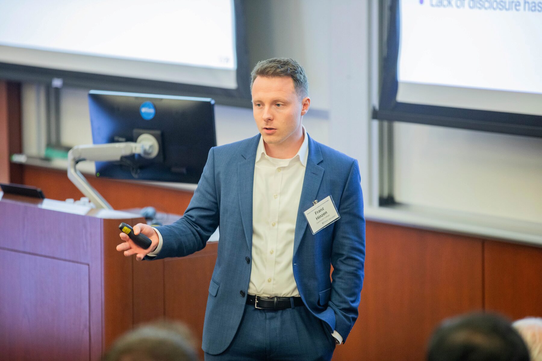 A conference speaker holds a remote clicker while addressing an audience