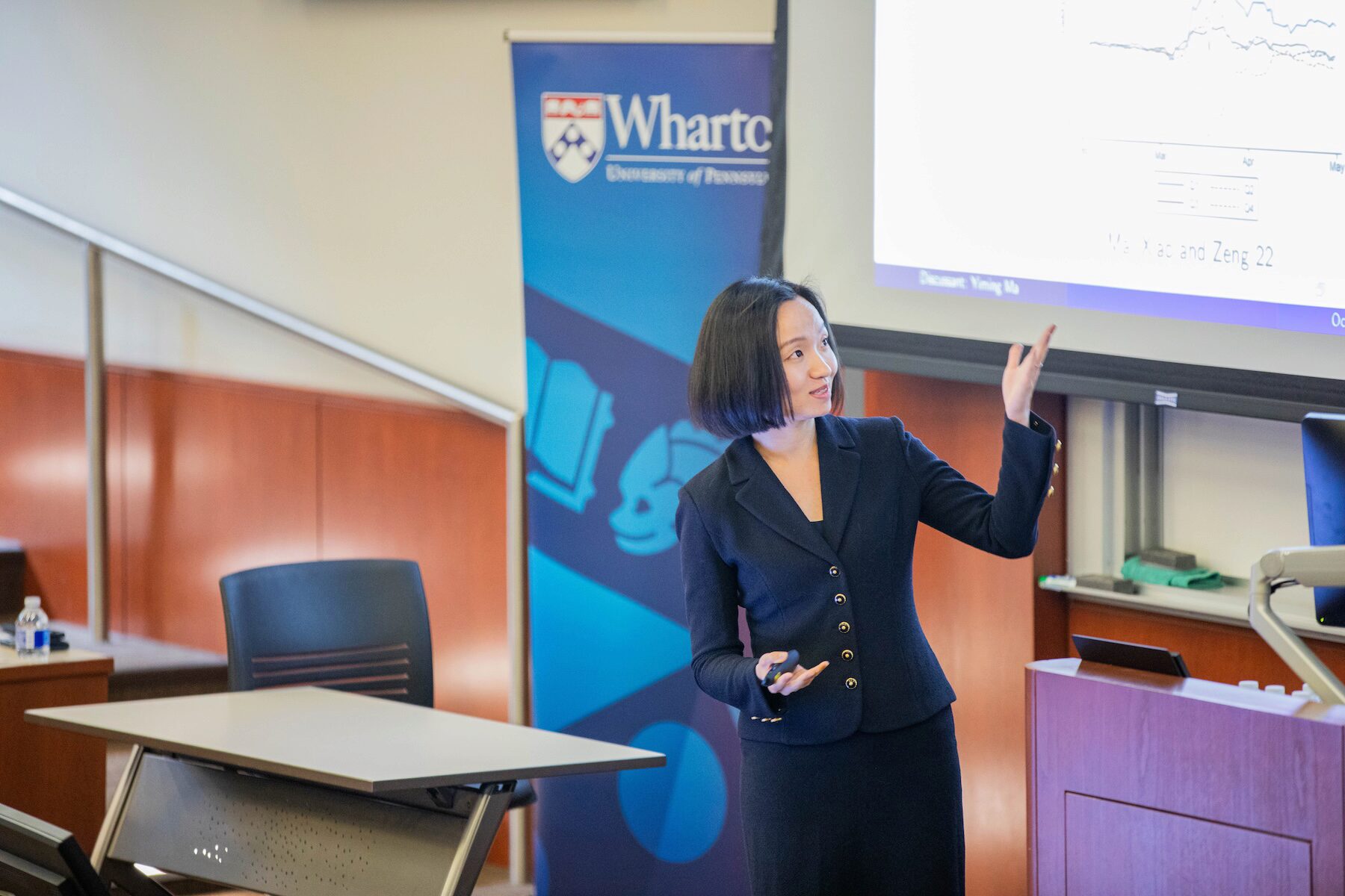 A speaker points toward a presentation screen during in a classroom setting