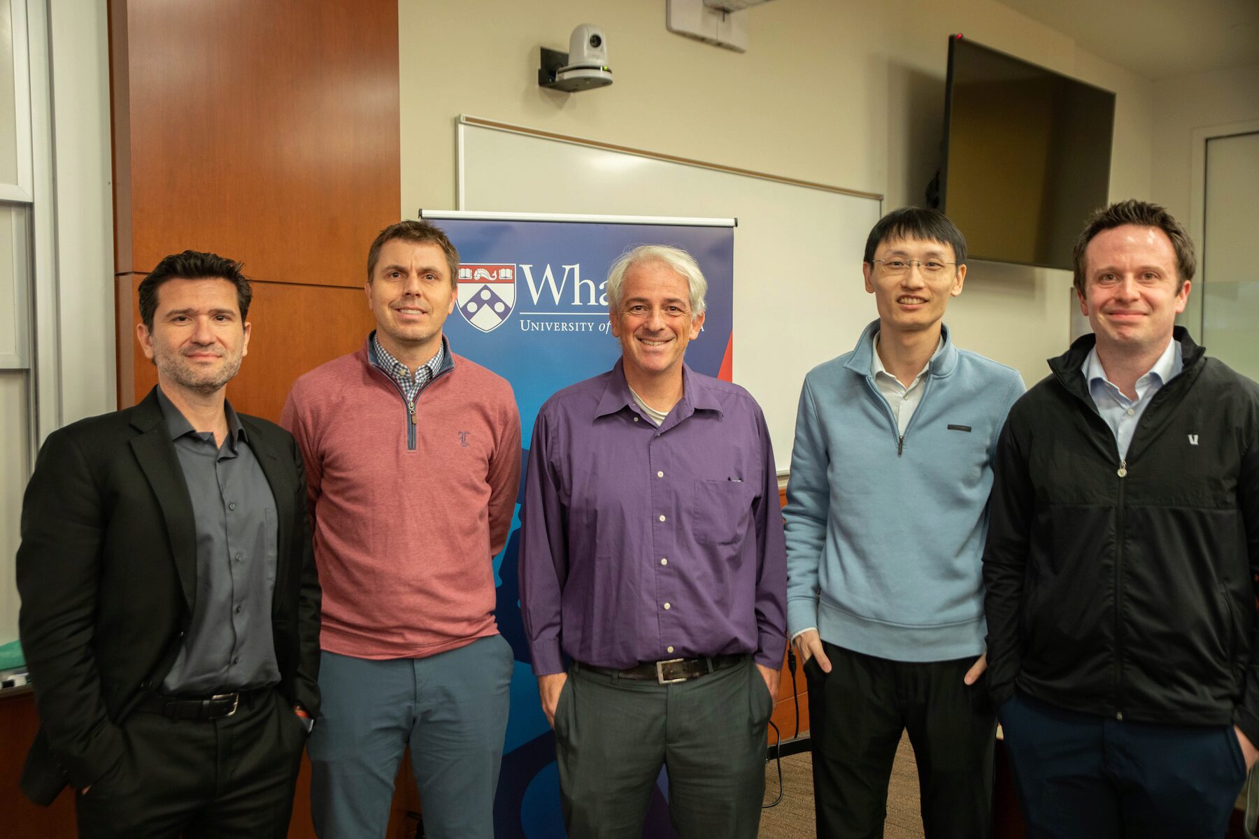 Five people pose for a group photo before a Wharton branded backdrop