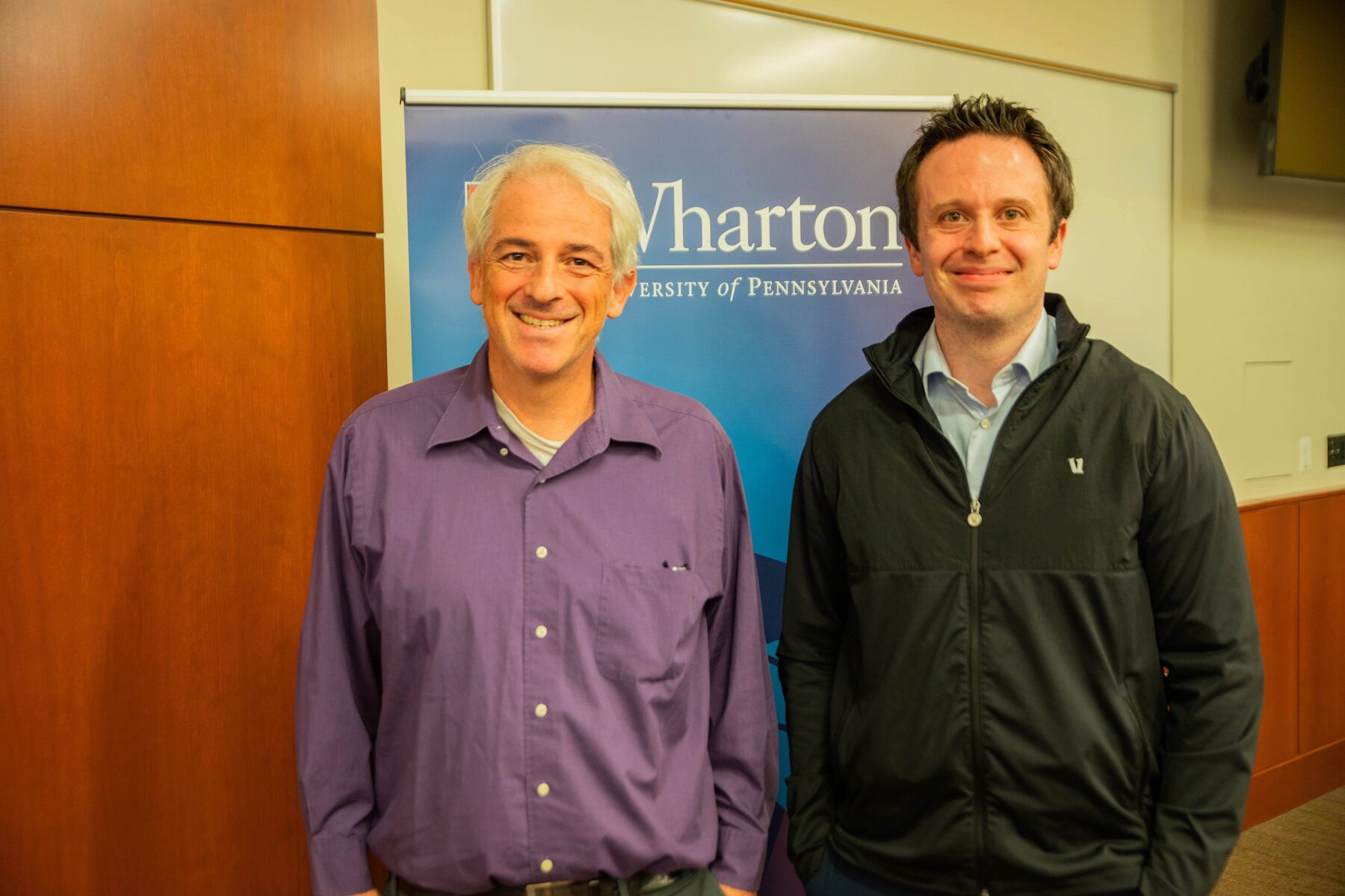 Two people pose for a group photo before a Wharton banner