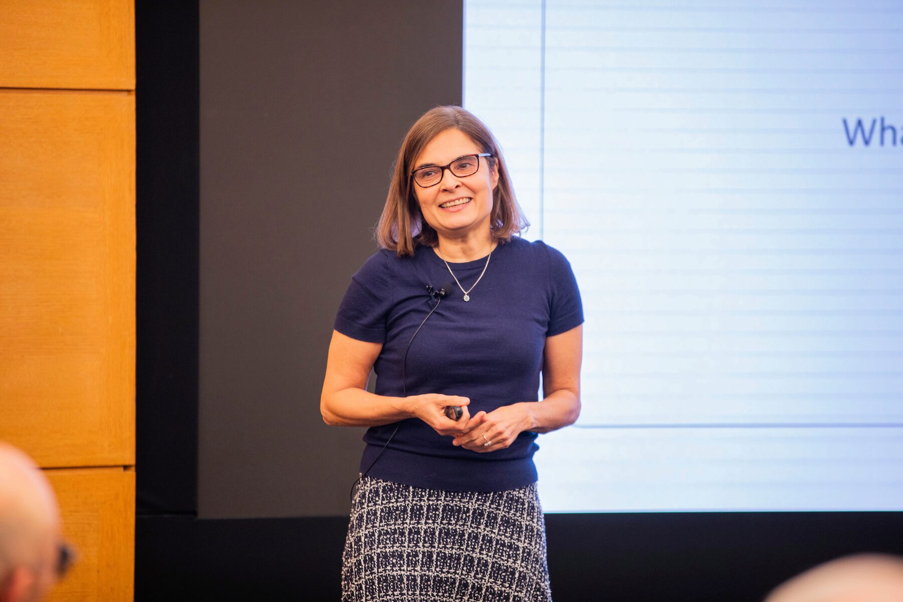 A speaker smiles during a presentation before a white screen